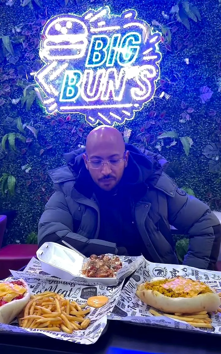 La salle de Big Bun’s : le néon Big Bun’s sur le mur végétal, un client devant les plateaux